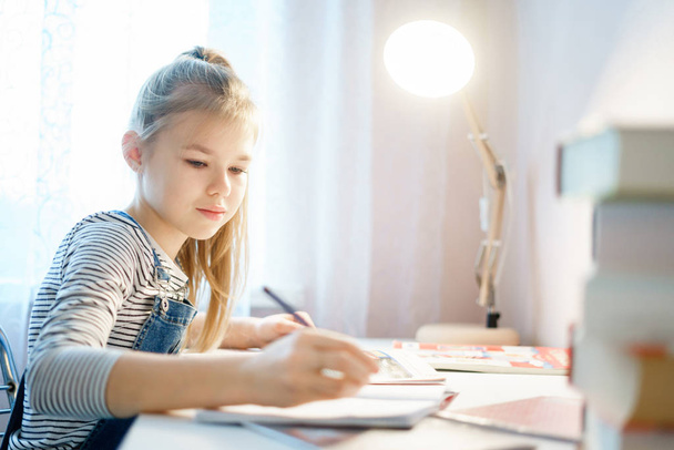 Девочка-подросток делает домашнюю работу за столом дома, готовится к школьному тесту
 - Фото, изображение