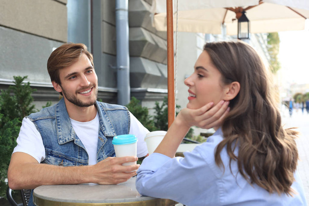 Attractive young couple in love drinking coffee while sitting at the cafe table outdoors. - Zdjęcie, obraz