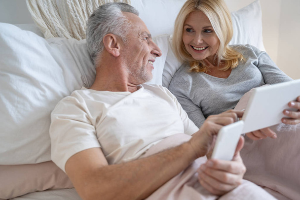 Mature couple with gadgets at home smiling stock photo - Photo, image