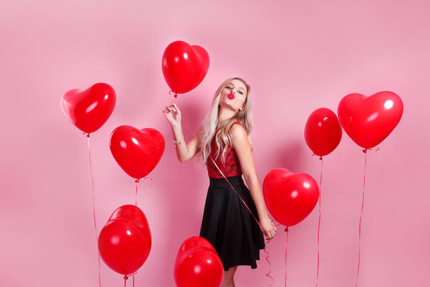 Beautiful emotional woman in elegant dress with red heart ballons on pink background - Foto, immagini