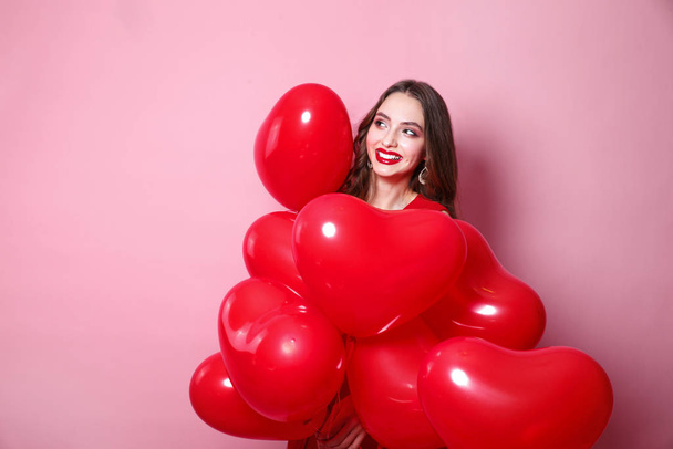 Beautiful elegant young woman with heart shape red air balloons on pink background. - Fotografie, Obrázek