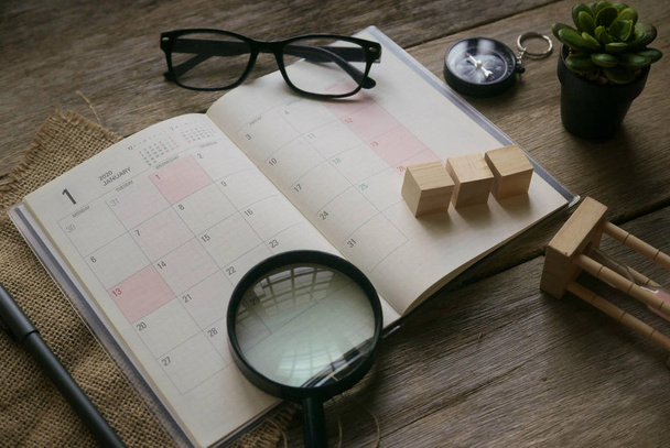 Draufsicht auf den Monat Januar 2020 Planer mit Brille, Kompass, Pflanze, Sanduhr, Lupe und Stift auf Holzgrund. - Foto, Bild