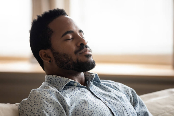Tranquil young african man resting eyes closed breathing on couch - Foto, Imagen