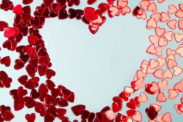 Red foil confetti arranged into a heart shaped frame on blue background. - Foto, imagen