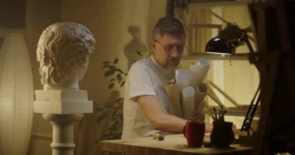 Umělec s role papíru sedí za stolem - Záběry, video