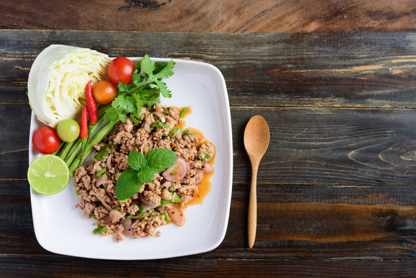 Thai food, spicy minced pork salad (Larb Moo) on white dish with spoon on wooden background, top view - Photo, Image