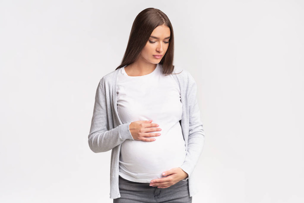 Pregnant Woman Looking Down Touching Belly Posing In Studio - Zdjęcie, obraz