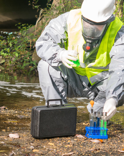 laboratory assistant in a protective suit and mask with a mini laboratory conducts an express test at the site of the alleged environmental pollution - Photo, image