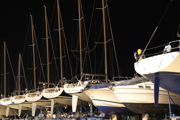 Overnight dry parking of yachts in the Croatian ACI marina of the town of Jazira. Burning lights of the evening Mediterranean port with sailing yachts and fishing boats. Twilight on the Adriatic - 写真・画像