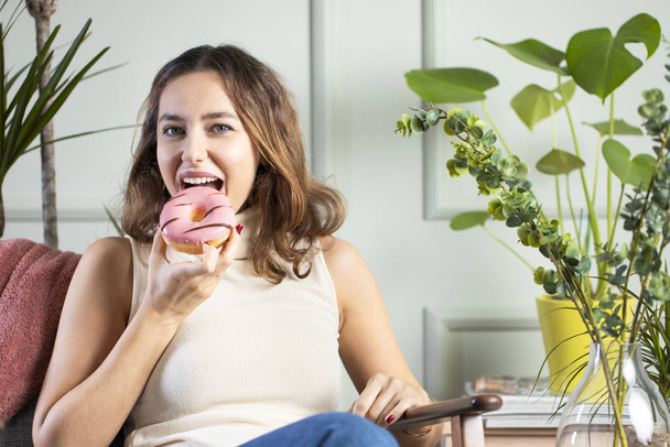 Young woman eating pink chocolate chips donut - Foto, immagini