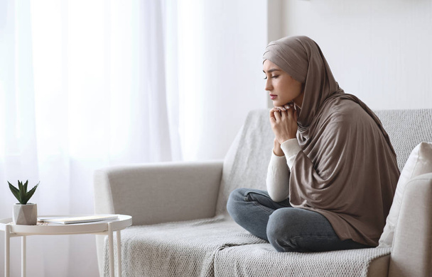 Mulher muçulmana deprimida no hijab sentado chateado no sofá em casa
 - Foto, Imagem
