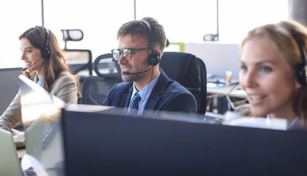 Portrait of call center worker accompanied by his team. Smiling customer support operator at work. - Фото, изображение