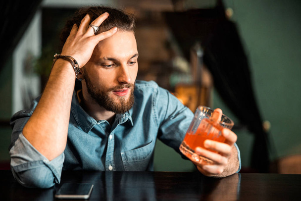 Nuori kaveri istuu alkoholijuoman kanssa baaritiskillä
 - Valokuva, kuva
