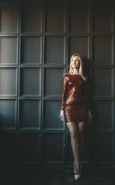 Mooi blond meisje in een korte rode jurk op een grijze alternatieve achtergrond in studio interieur. - Foto, afbeelding