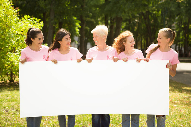 Nők rózsaszín pólóban, üres poszterrel a parkban. - Fotó, kép