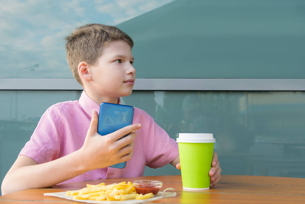 Ένα αγόρι με πουκάμισο τρώει και χρησιμοποιεί ένα μαραφέτι ενώ τρώει. - Φωτογραφία, εικόνα