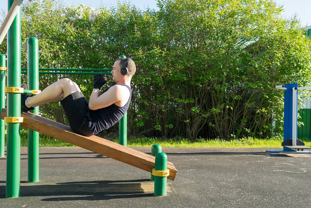 a man on the sports ground does an exercise on the press and listens to music through headphones - Fotó, kép