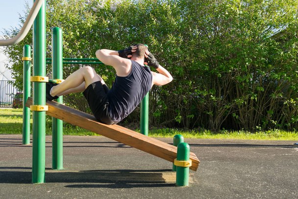 side view of a man on the sports ground doing an abs exercise and listening to music through headphones - Foto, imagen