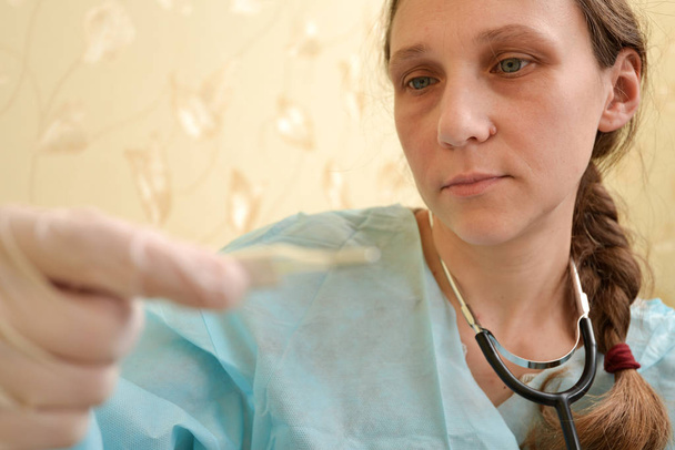Kobieta lekarz patrzy na termometr, aby określić wysoką temperaturę dla choroby pacjenta. - Zdjęcie, obraz