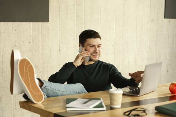 Młody człowiek rozmawia przez telefon Siedząc na laptopie w biurze - Zdjęcie, obraz