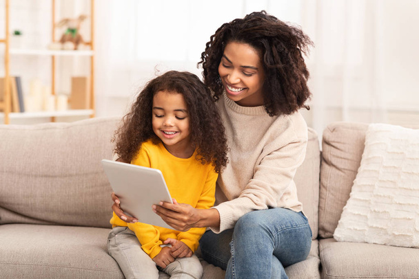 Moeder en dochter met behulp van tablet kijken cartoons zitten op de bank - Foto, afbeelding