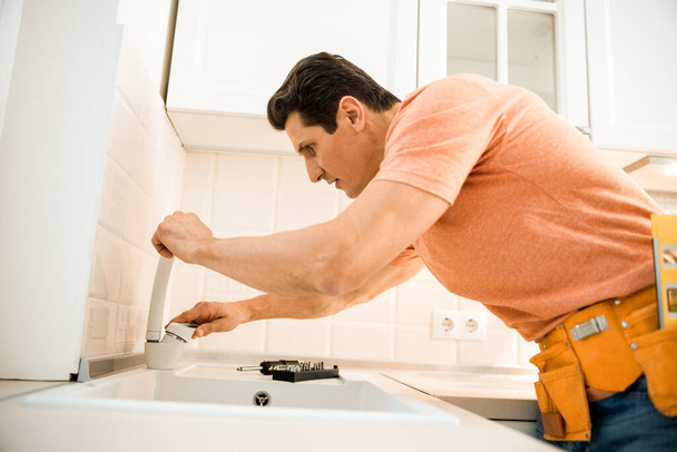 Adult worker using screwdriver while repairing faucet in the kitchen - Zdjęcie, obraz