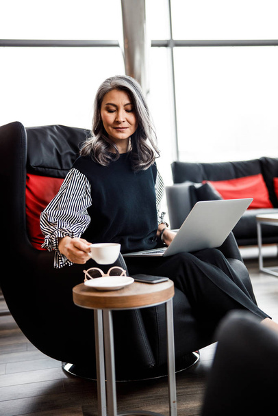 Beautiful woman with laptop and coffee in armchair stock photo - Φωτογραφία, εικόνα