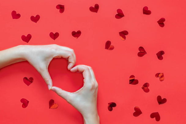 Vrouw handen maken hart vorm op rode achtergrond met rode harten - Foto, afbeelding