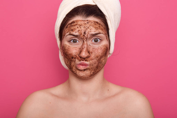 Dissatisfied young woman doesnt like smell from beauty mask, doing procedures for removing wrinkles on face, wearing white towel and standing with bare shoulders isolated over pink studio wall. - Foto, Bild