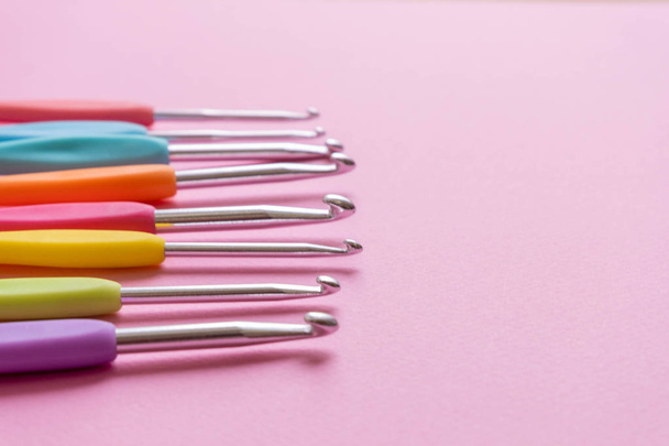 Closeup image of different size colorful crochet hooks on soft pink background - Photo, image