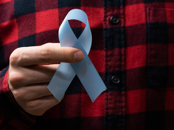 Concept of medicine and means of health care. A man in a plaid shirt holds a blue ribbon. A sign of the fight against prostate cancer - 写真・画像