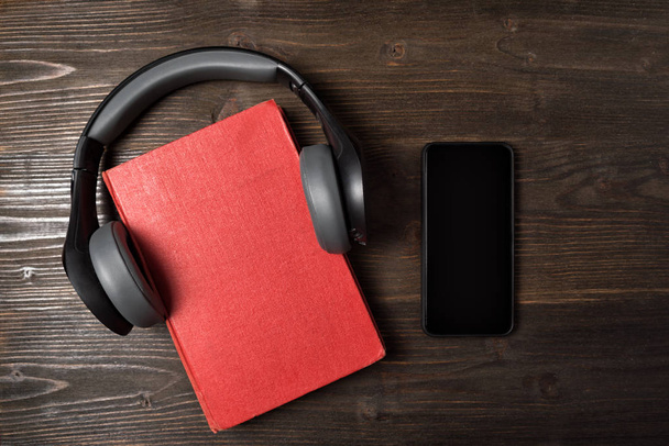 Libro rojo, auriculares y teléfono sobre fondo de madera. Concepto de audiolibros. Vista superior
 - Foto, Imagen