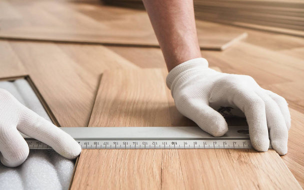 Installing laminated floor, detail on man hands holding metal ruler over wooden tile, white foam base layer under - Фото, изображение
