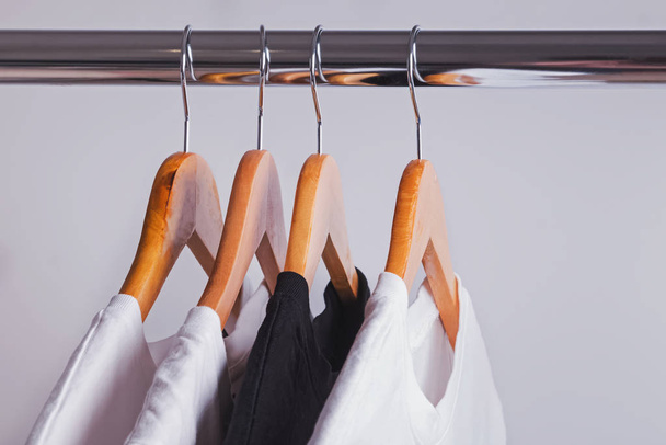 One black t-shirt in a row of white shirts hanging on wooden hangers - Foto, Imagem