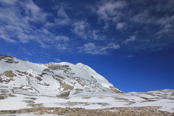 Χιονισμένα βουνά ενάντια στον γαλάζιο ουρανό με άσπρα σύννεφα. Όρος - Φωτογραφία, εικόνα