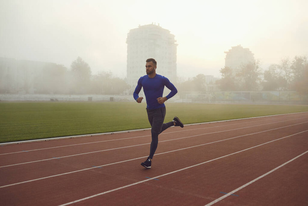 A young athlete runs on a stadium in the fog. - Zdjęcie, obraz