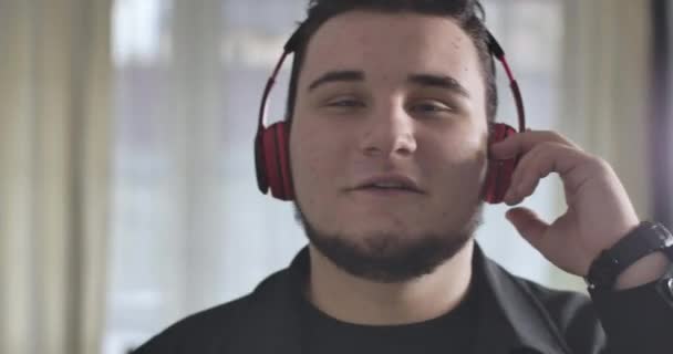 Close-up portrait of plump Caucasian man enjoying music in headphones. Happy young guy listening to music in earphones. Cinema 4k ProRes HQ. - Materiał filmowy, wideo