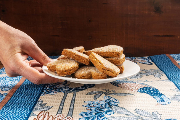 Uma mão feminina coloca um prato de biscoitos em uma mesa. A mesa está coberta com um pano
. - Foto, Imagem