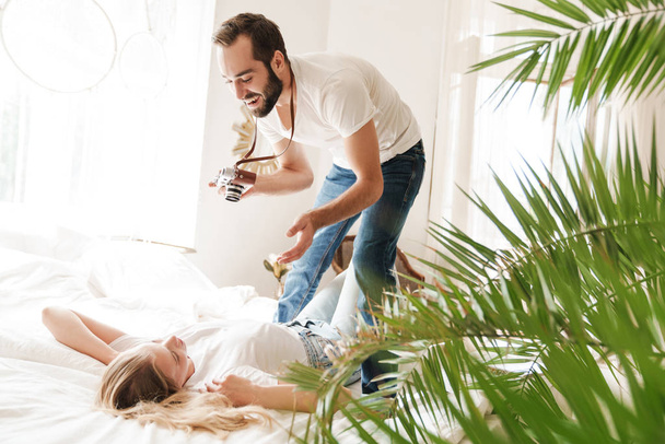 Cheerful young couple taking photos indoors while laying on bed - Φωτογραφία, εικόνα