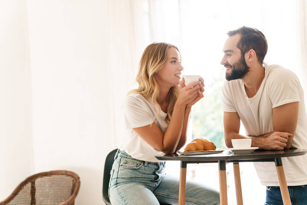 Happy beautiful young couple having breakfast at the kitchen table - Foto, Imagen