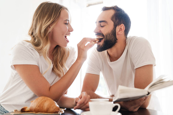 Happy beautiful young couple having breakfast at the kitchen table - Foto, Imagem