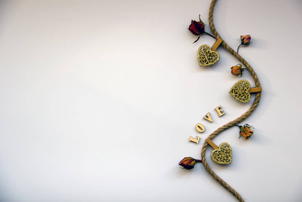 The word love made of wooden letters, wooden hearts pinned on twine, dry rose buds on a white background. Love concept. Valentines day concept. Top view, flat lay, copy space. - Photo, Image