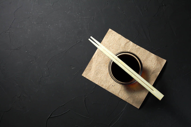 Chopsticks lie on soy sauce, dark background, place for an inscription - Foto, afbeelding