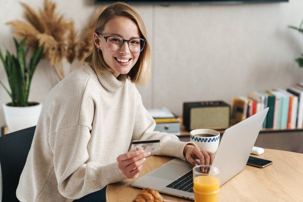 Photo of joyful blonde woman holding credit card and using laptop - Foto, Imagem