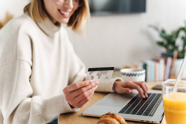 Photo of joyful attractive woman holding credit card and using laptop - Foto, Imagem