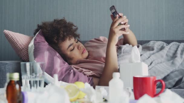 Nemocný mladý africký americký dívka pomocí telefonu a foukání nos s kapesníkem - Záběry, video