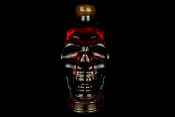 Glasflasche in Form eines Totenkopfes mit Alkohol im Inneren, rot leuchtend auf schwarzem Hintergrund - Foto, Bild