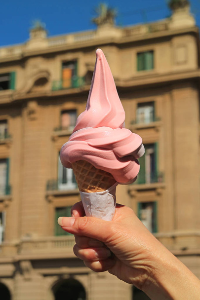 Cône de crème glacée de couleur rose Raspberry Soft Serve tenu à la main, avec un bâtiment vintage flou à Santiago du Chili en arrière-plan
 - Photo, image