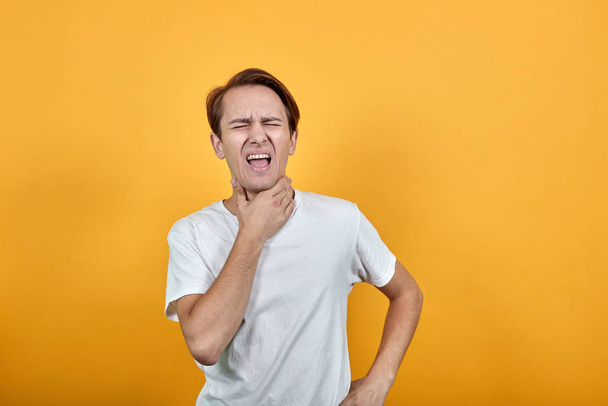 Man met zere keel zere keel vasthouden aan zijn nek op gele achtergrond - Foto, afbeelding