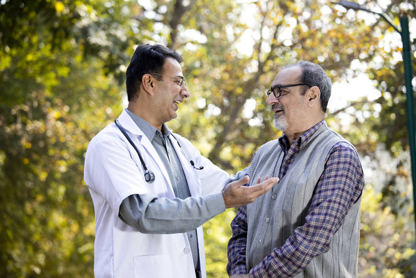Doctor hablando con el hombre mayor en el jardín del hospital
 - Foto, Imagen